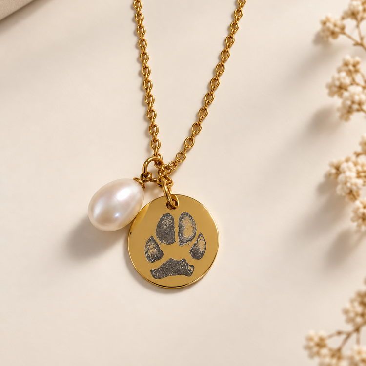 Gold pawprint necklace with an engraved dog paw print disc and a natural pearl charm