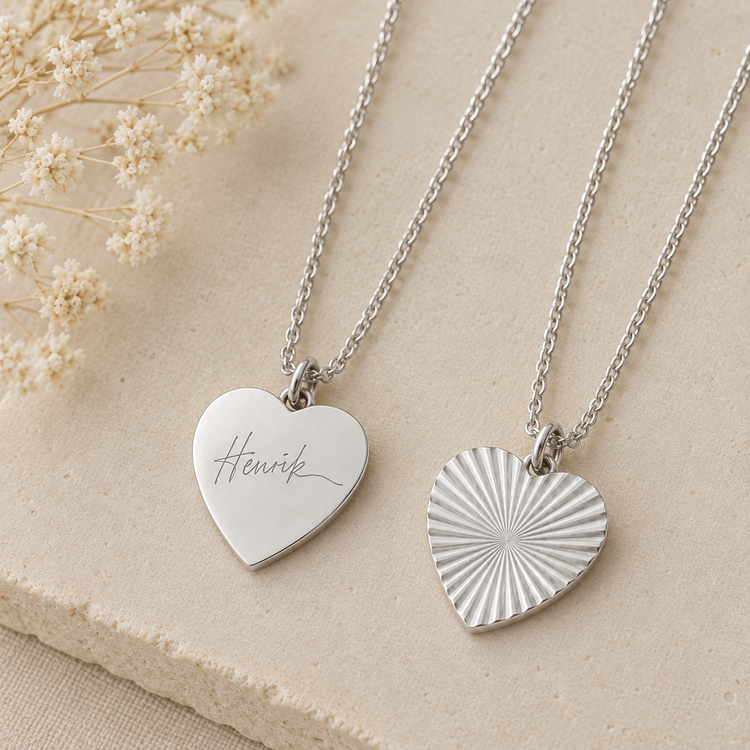 Silver heart necklace engraved with a handwritten signature beside the sunburst side