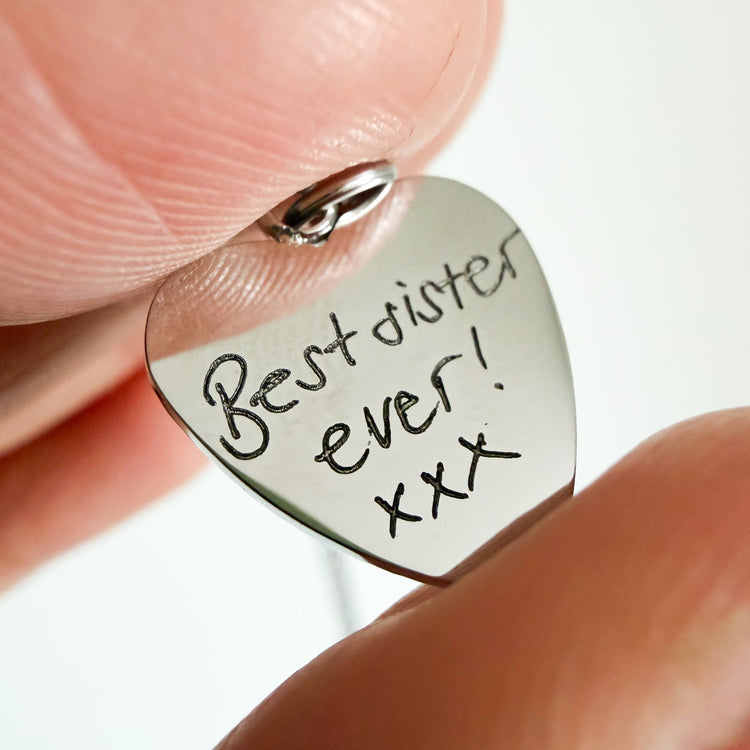 Close-up of a silver heart charm engraved with handwritten 'Best sister ever! xxx'