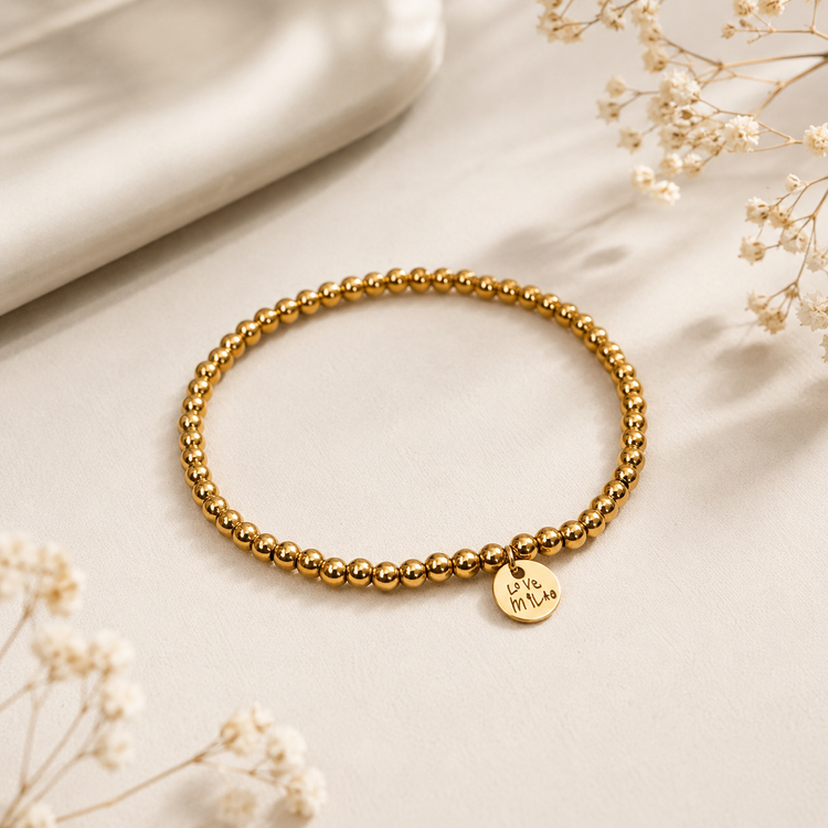 Gold beaded bracelet with a heart-shaped tag which is engraved