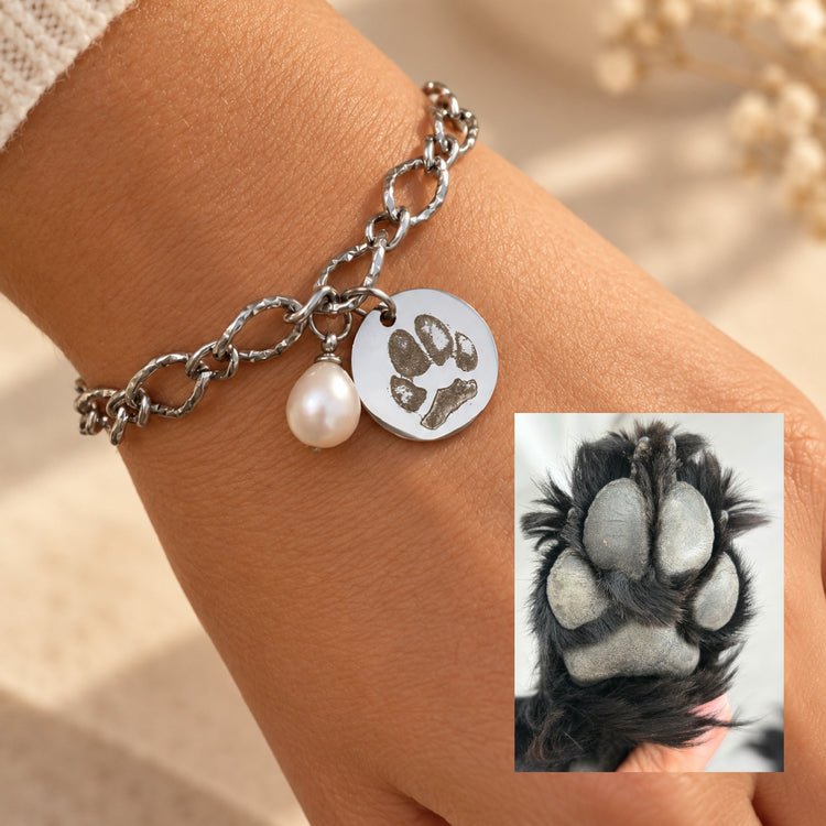 Silver pawprint bracelet worn on the wrist, engraved with a dog's paw print shown beside the original