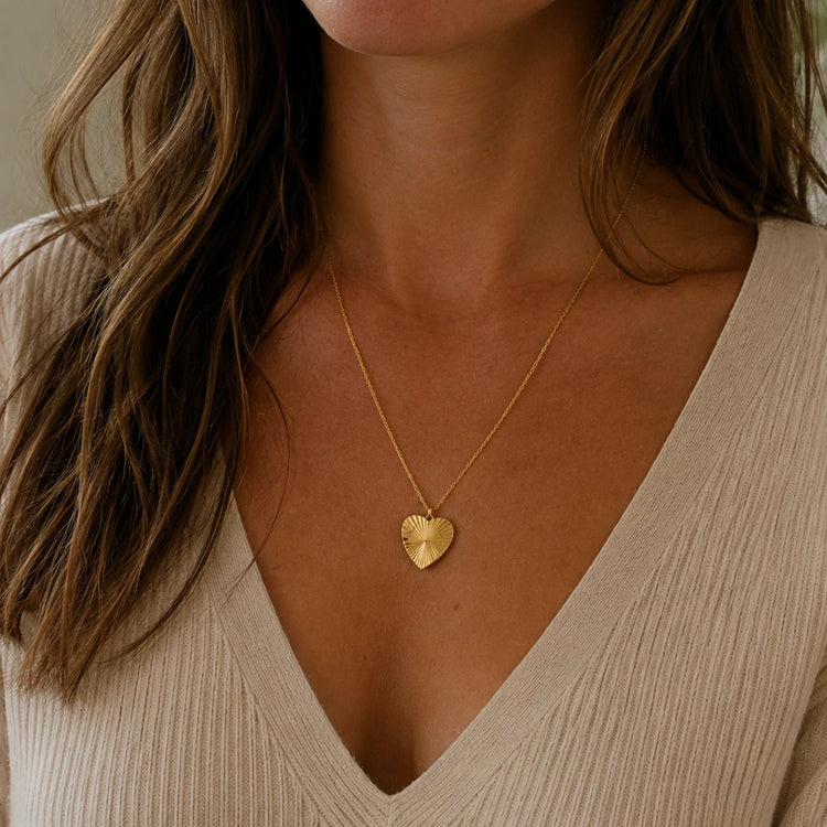Woman wearing a gold sunburst heart necklace engraved with handwriting