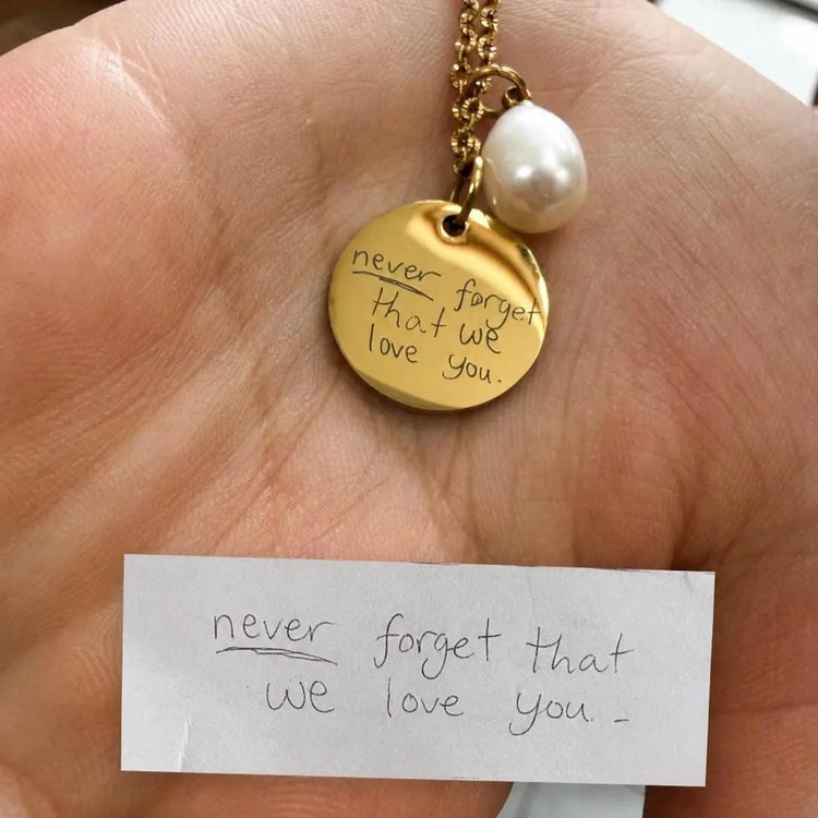 A gold disc pendant necklace with a white pearl charm and custom handwriting engraved