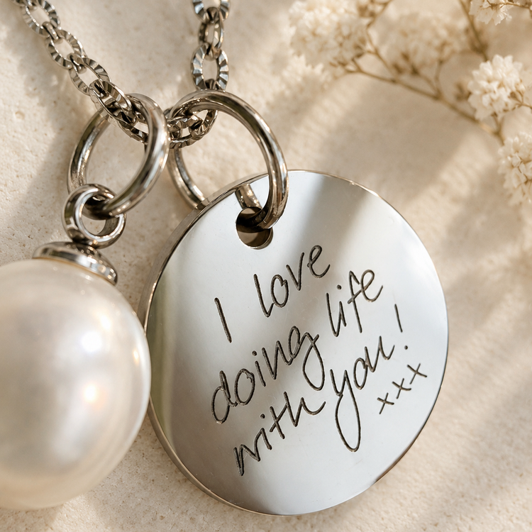 Close-up of a silver pendant engraved with handwritten 'I love doing life with you' next to an optional pearl charm