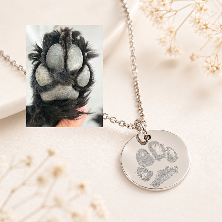 Silver custom pawprint necklace with a round pendant engraved with a dog's real paw print, beside the original paw photo